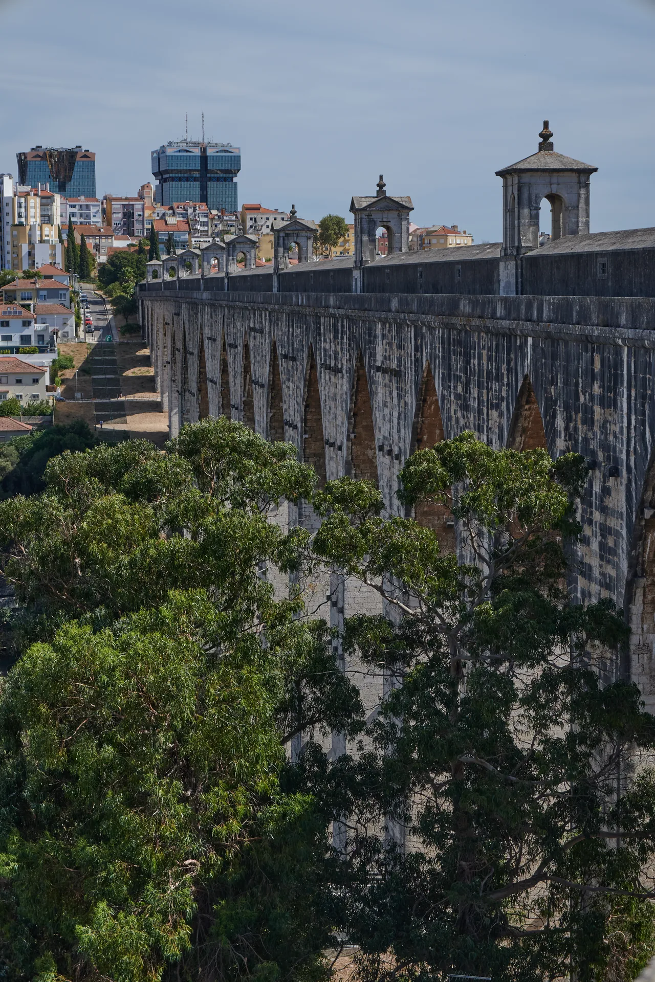 Stone arches and roofed turrets of the Águas Livres Aqueduct above trees and city buildings