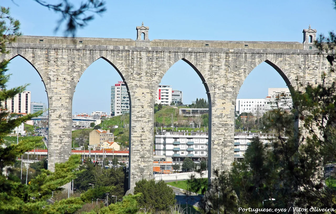 Tall pointed arches of the Águas Livres Aqueduct with buildings behind them