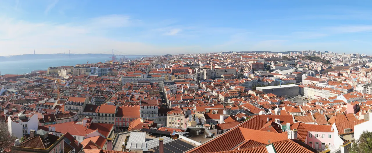 Red roofs across central Lisbon, with the Tagus and 25 de Abril Bridge beyond, seen from São Jorge Castle.