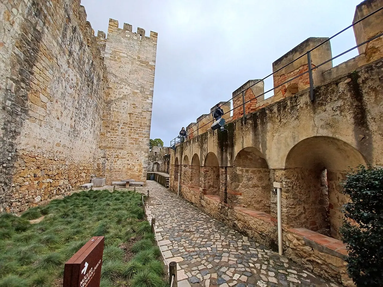 A cobbled passage between São Jorge Castle’s walls and an elevated wall walk.
