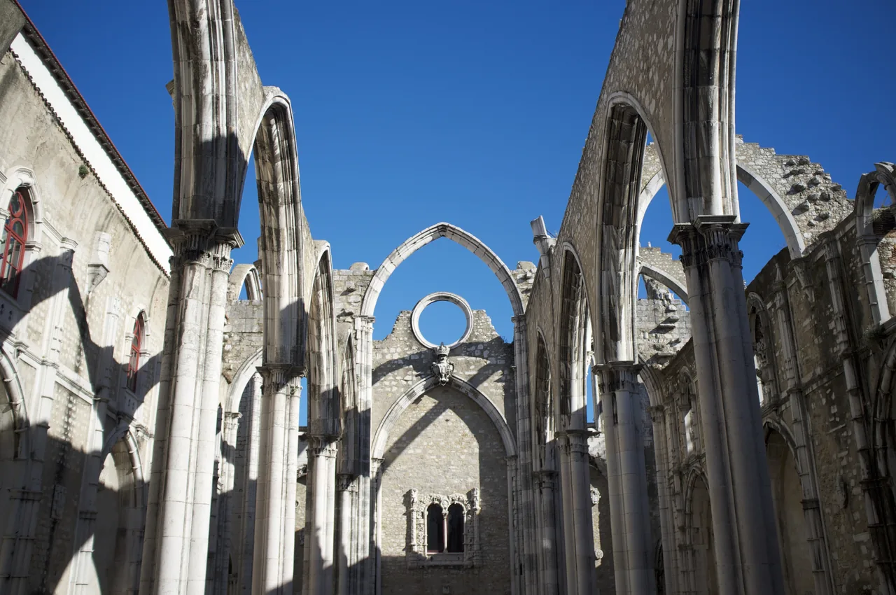 Stone arches above the roofless nave of Carmo Convent beneath a clear blue sky.
