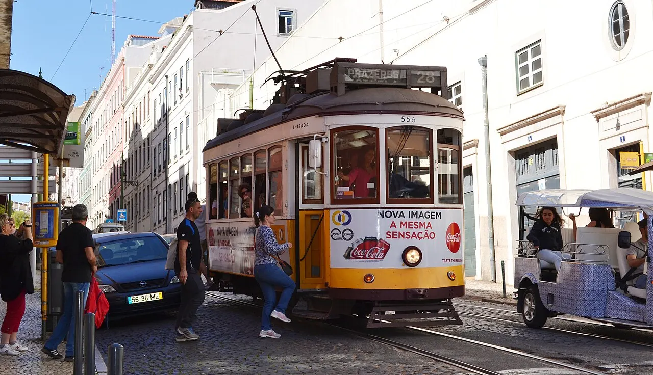 A passenger stepping up into the doorway of a historic Lisbon Tram 28.