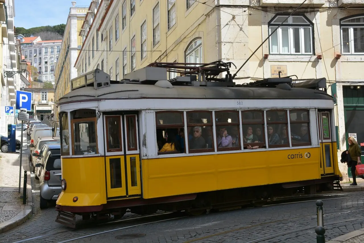 A yellow Lisbon tram rounding a tight corner between pale buildings near the cathedral.