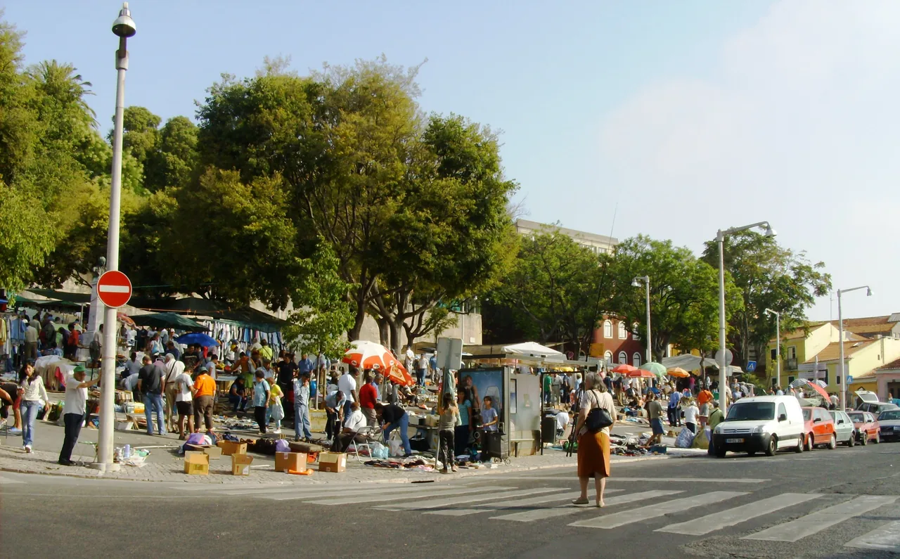 Visitors browse outdoor stalls beneath trees at Feira da Ladra