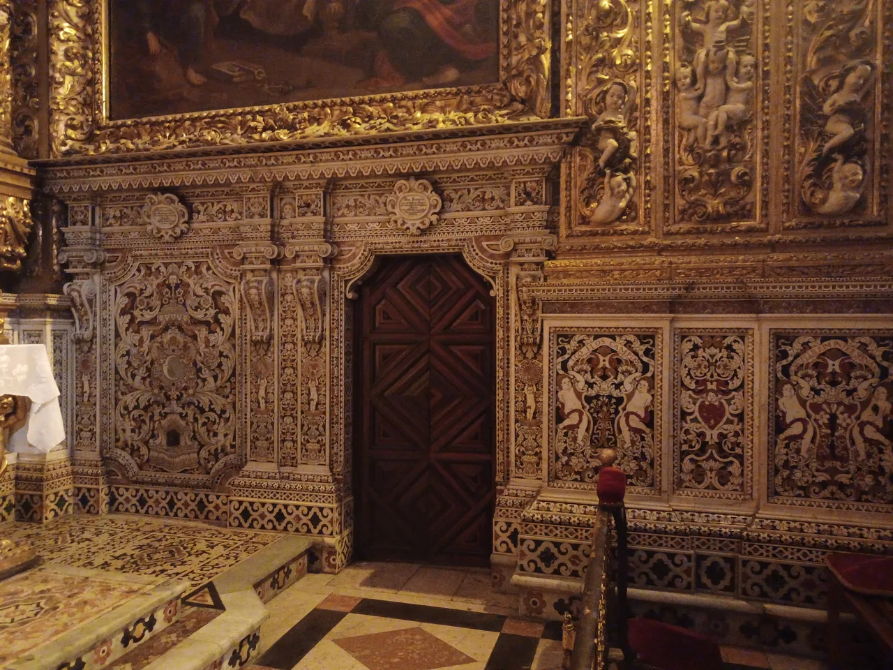 Talha dourada, pinturas emolduradas e trabalho em pedra com padrões numa capela de São Roque.