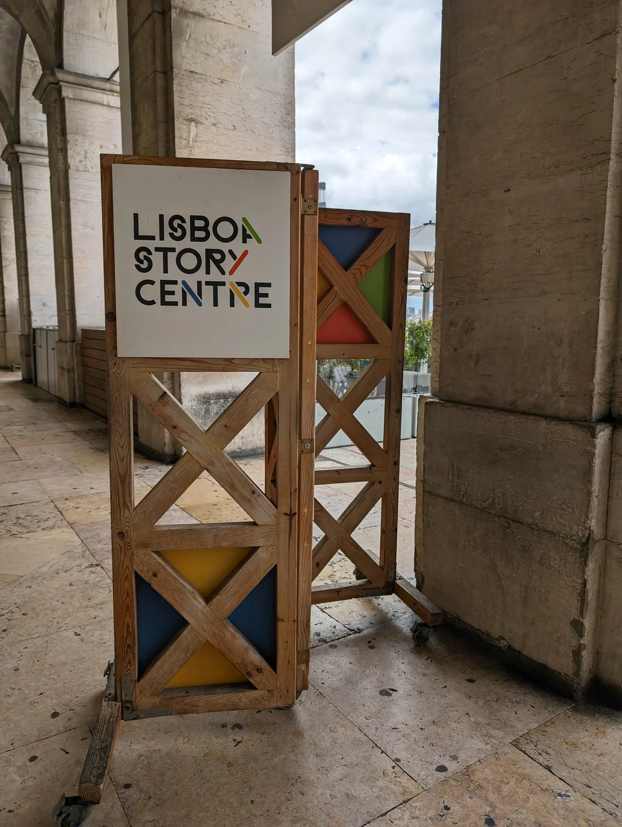 Lisboa Story Centre sign beneath the stone arcades of Praça do Comércio