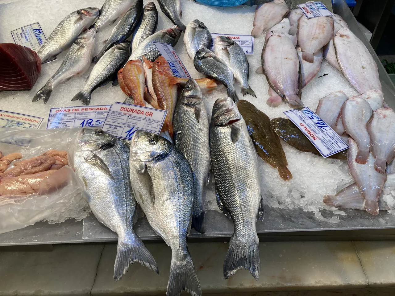 Peixes inteiros expostos sobre gelo numa banca de peixe do Mercado da Ribeira.