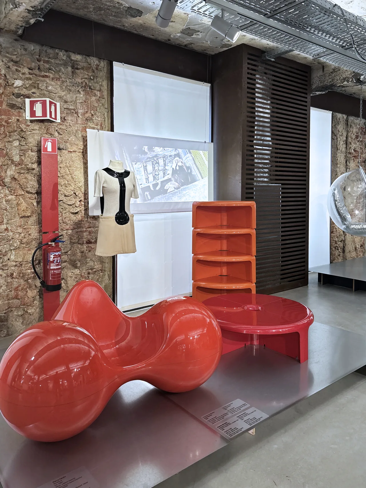 Red sculptural chair and low table with a fashion display behind them at MUDE