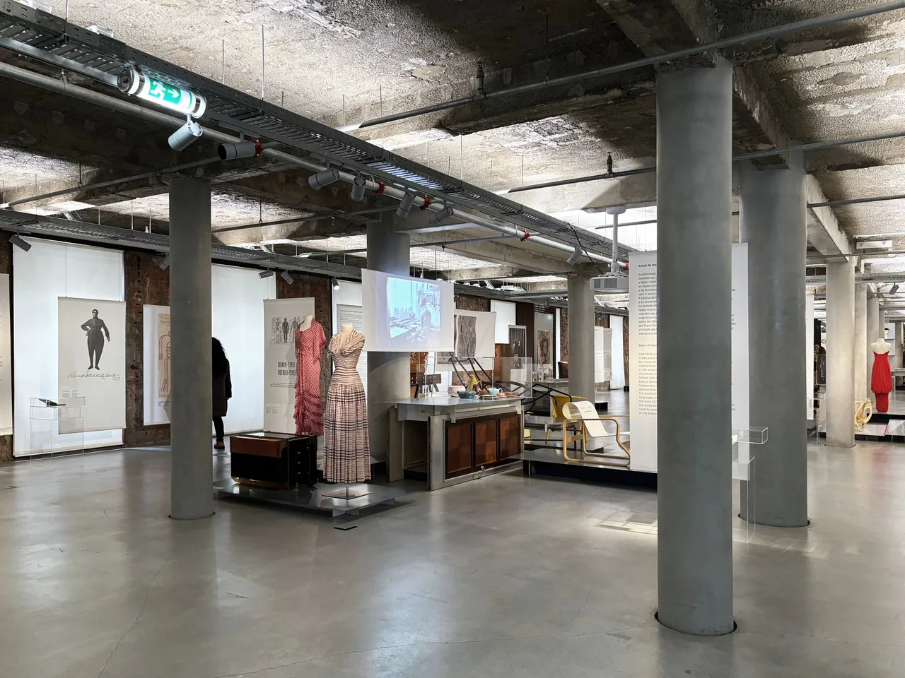 Furniture displayed across an open gallery beneath exposed concrete at MUDE