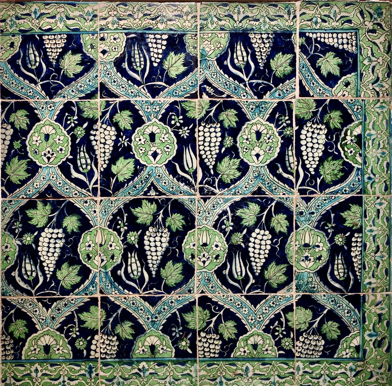 A patterned tile panel with flowers, leaves and curling stems in blue, green and white.