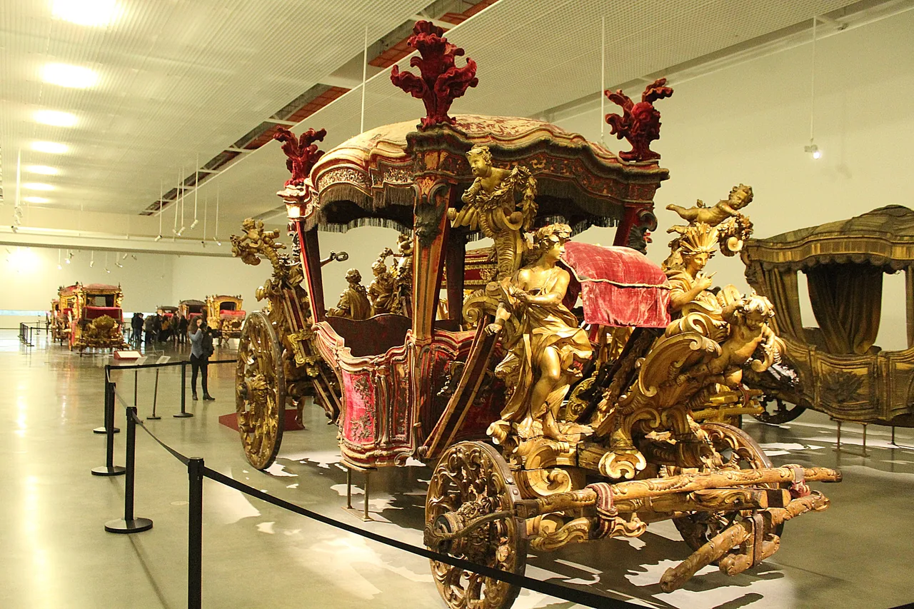 Um coche cerimonial ornamentado, com figuras esculpidas e decoração dourada, no Museu Nacional dos Coches.