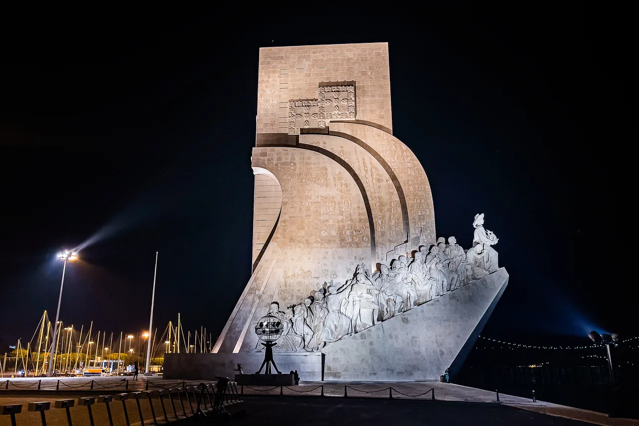 The illuminated stone sail and sculpted figures of the Monument to the Discoveries against the night sky.