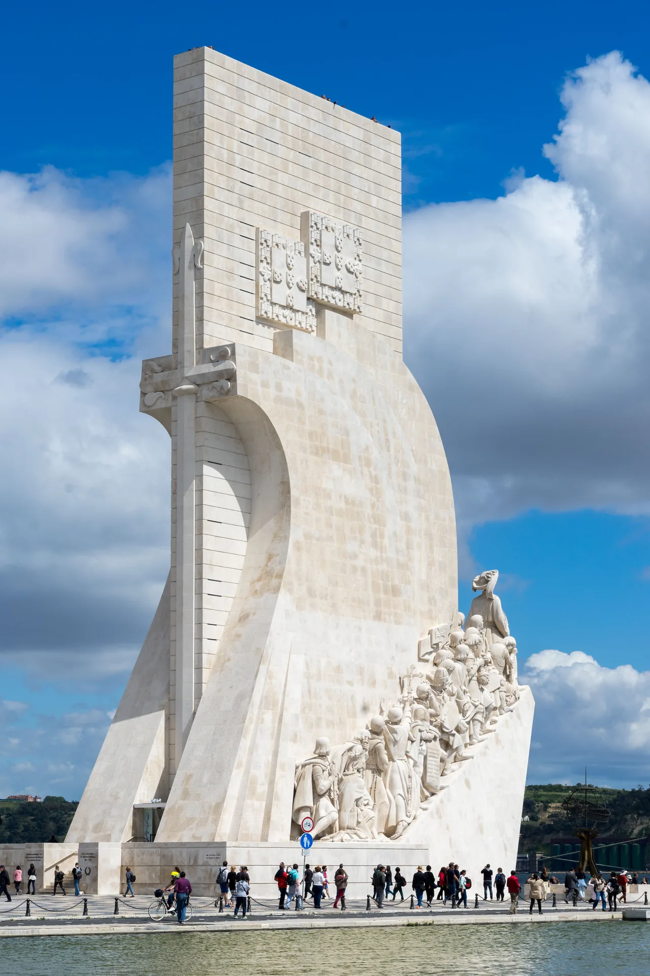 The sail-shaped tower and sculpted figures of the Monument to the Discoveries against a blue sky.