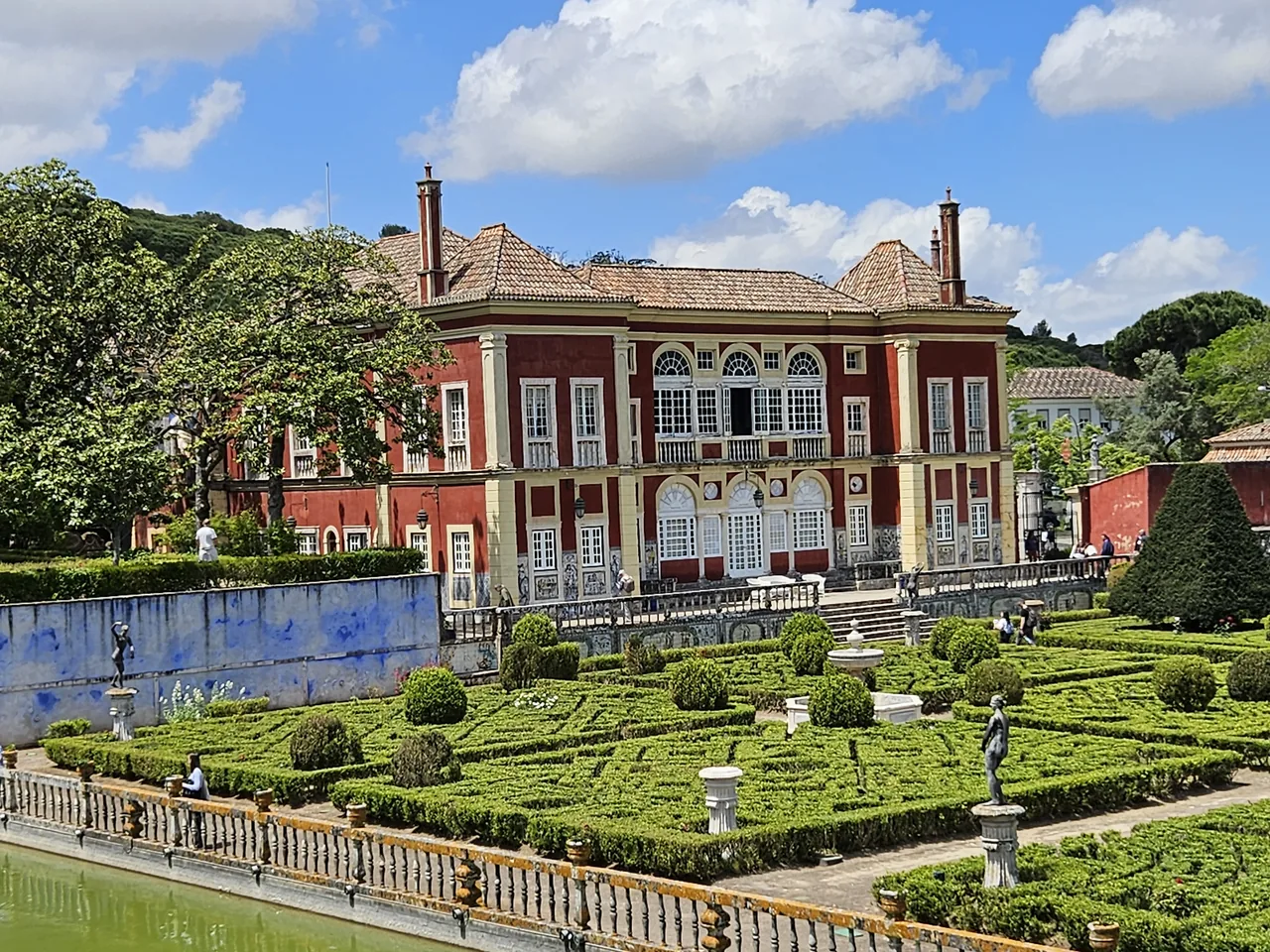 Red façade of Fronteira Palace beyond clipped hedges and tiled garden walls
