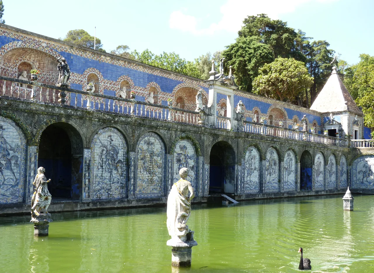 Galería de arcos con azulejos y esculturas reflejadas en el agua verde del estanque del Palacio de Fronteira