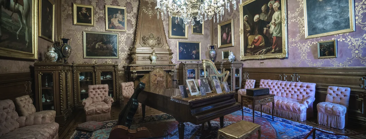 Framed paintings, upholstered chairs and a writing table in a sitting room at Ajuda Palace.