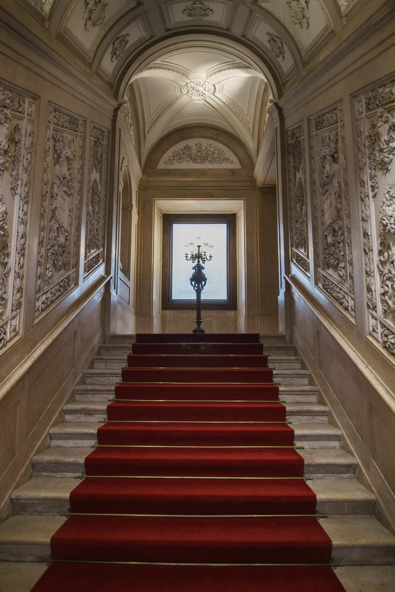 A red-carpeted staircase beneath a tall vaulted ceiling at Ajuda Palace.