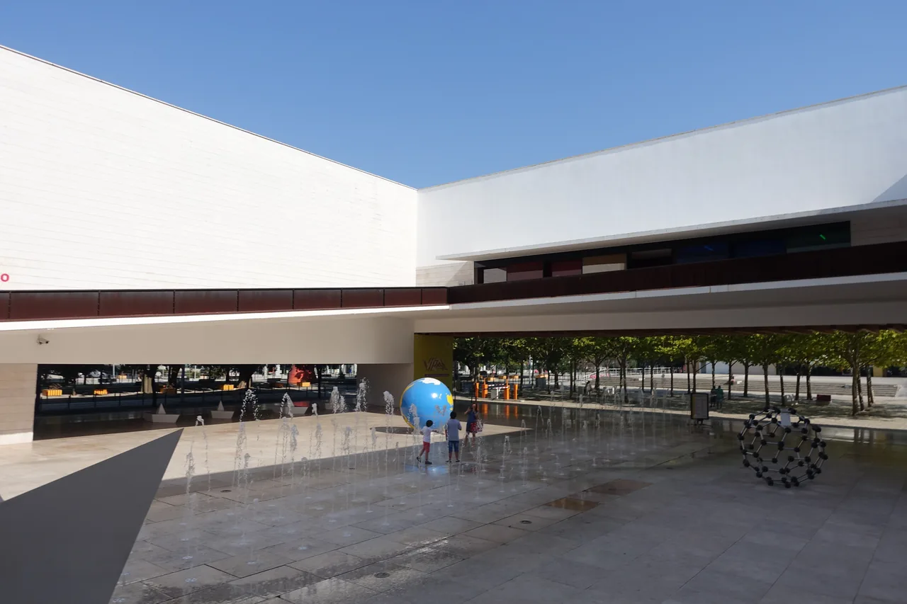 Broad entrance court beneath the projecting white wing of Pavilhão do Conhecimento