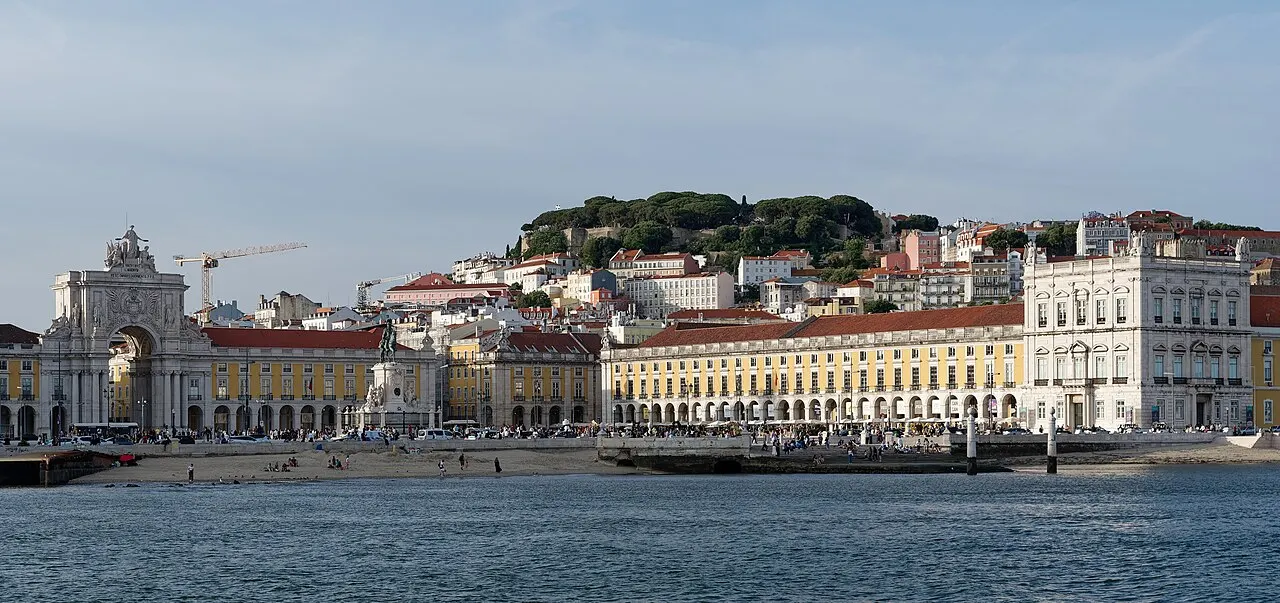 Praça do Comércio’s arcades and the Rua Augusta arch seen across the Tagus, with the castle hill behind.