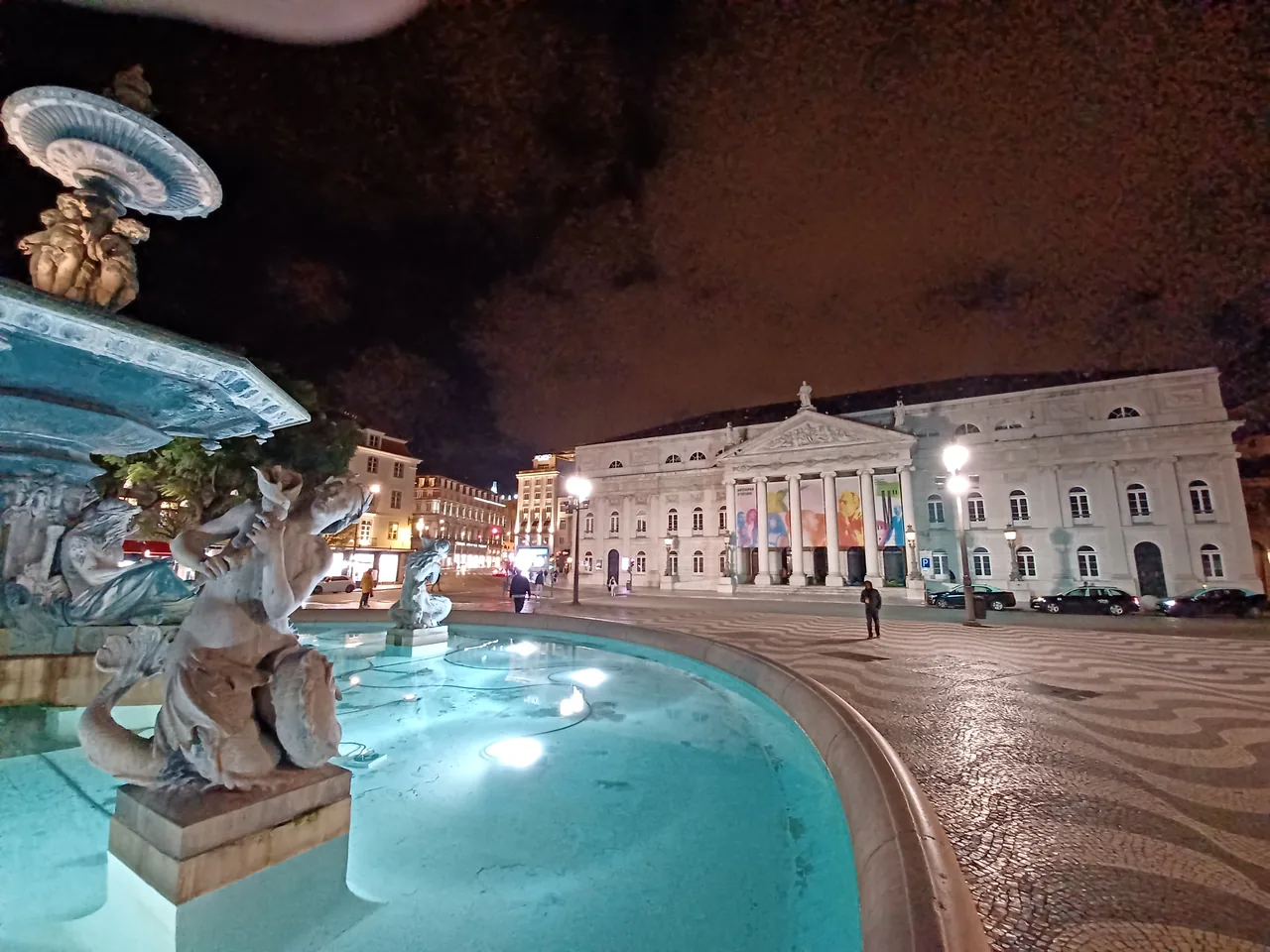 Una fuente iluminada y los edificios de alrededor en Rossio por la noche.
