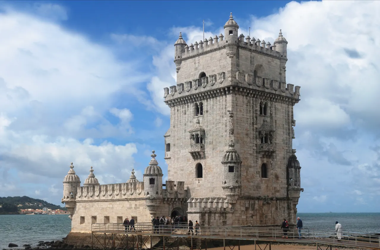 Belém Tower’s stone bastion and corner turrets beside the Tagus, with visitors on the footbridge.