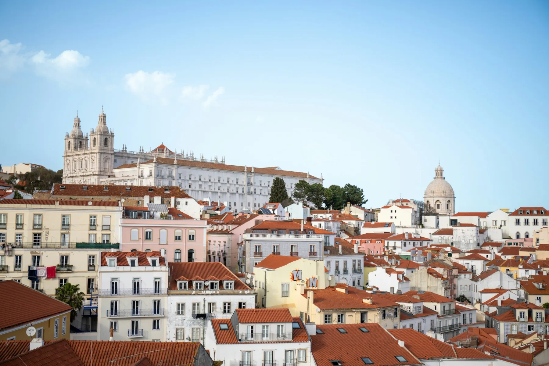 Alfama rooftops and historic monuments beneath a blue Lisbon sky
